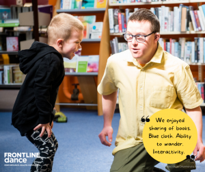 White Male Explorer who has Down syndrome wears yellow and green interacting. with an audience member- young boy.