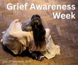 Two women are sitting on a wooden floor, with one holding the other. Photo taken from behind